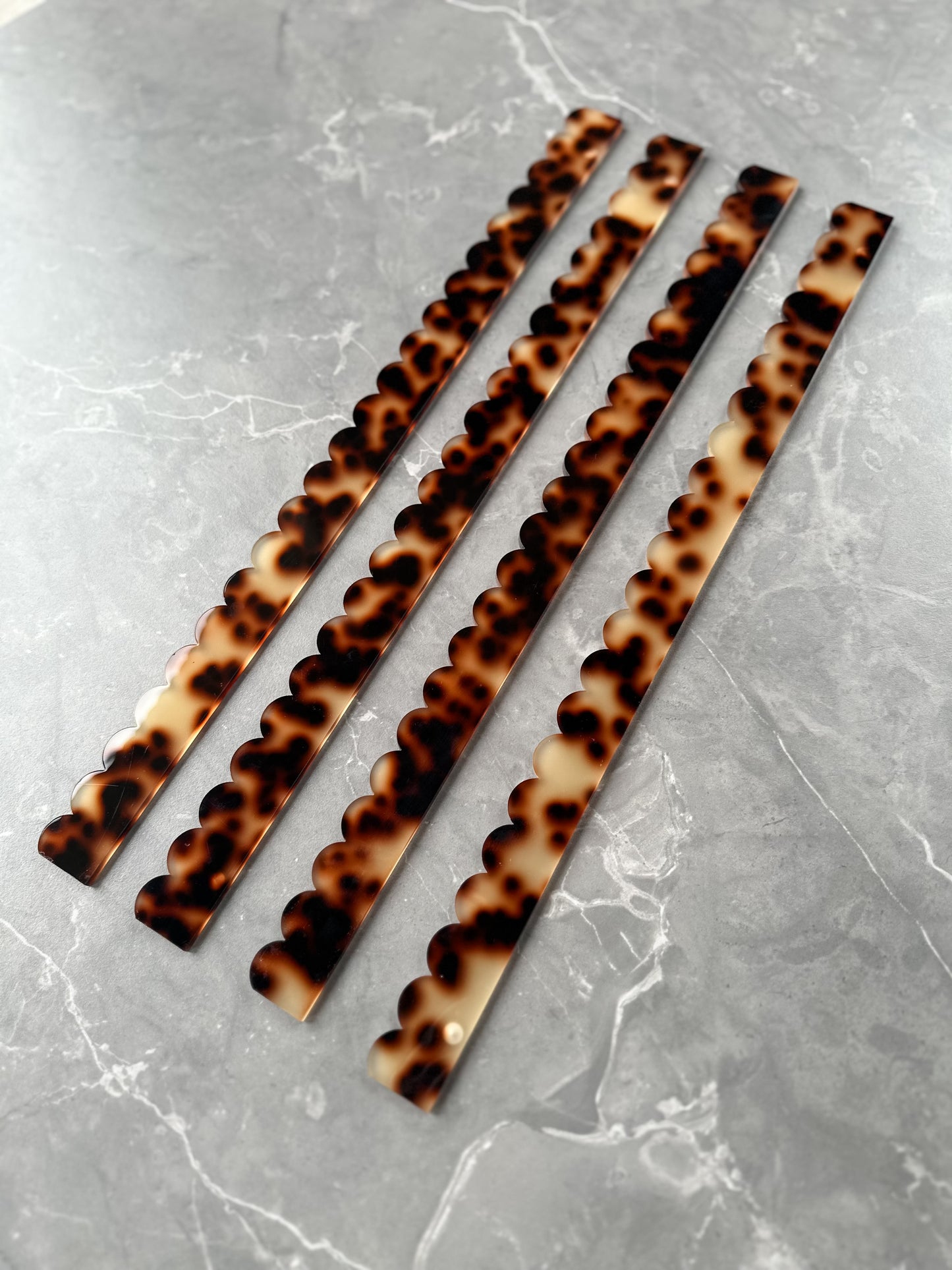 Set of four Mahj Mood tortoise acrylic scalloped mahjong pushers fanned diagonally on grey marble showing tortoiseshell pattern and scalloped design