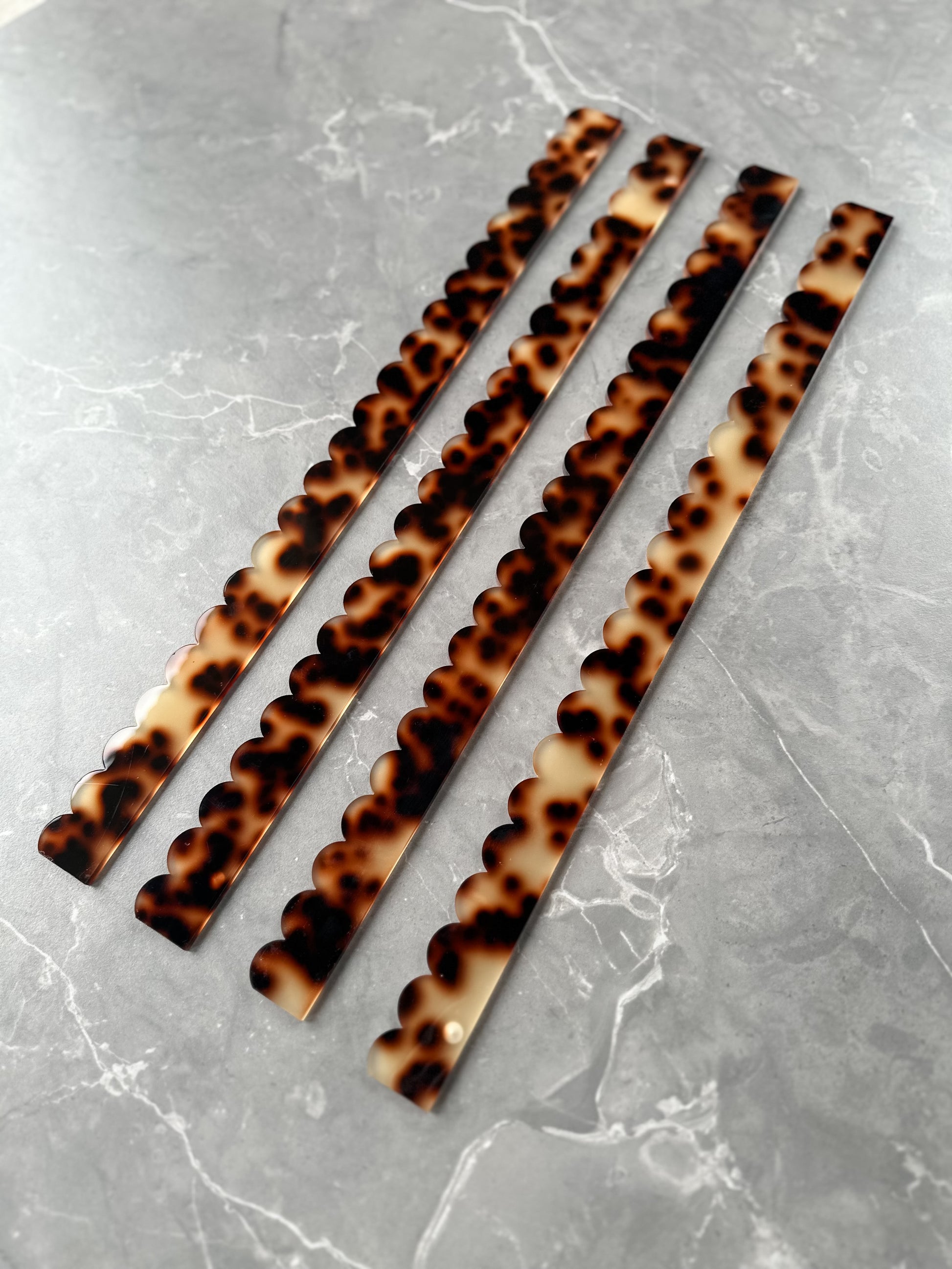 Set of four Mahj Mood tortoise acrylic scalloped mahjong pushers fanned diagonally on grey marble showing tortoiseshell pattern and scalloped design