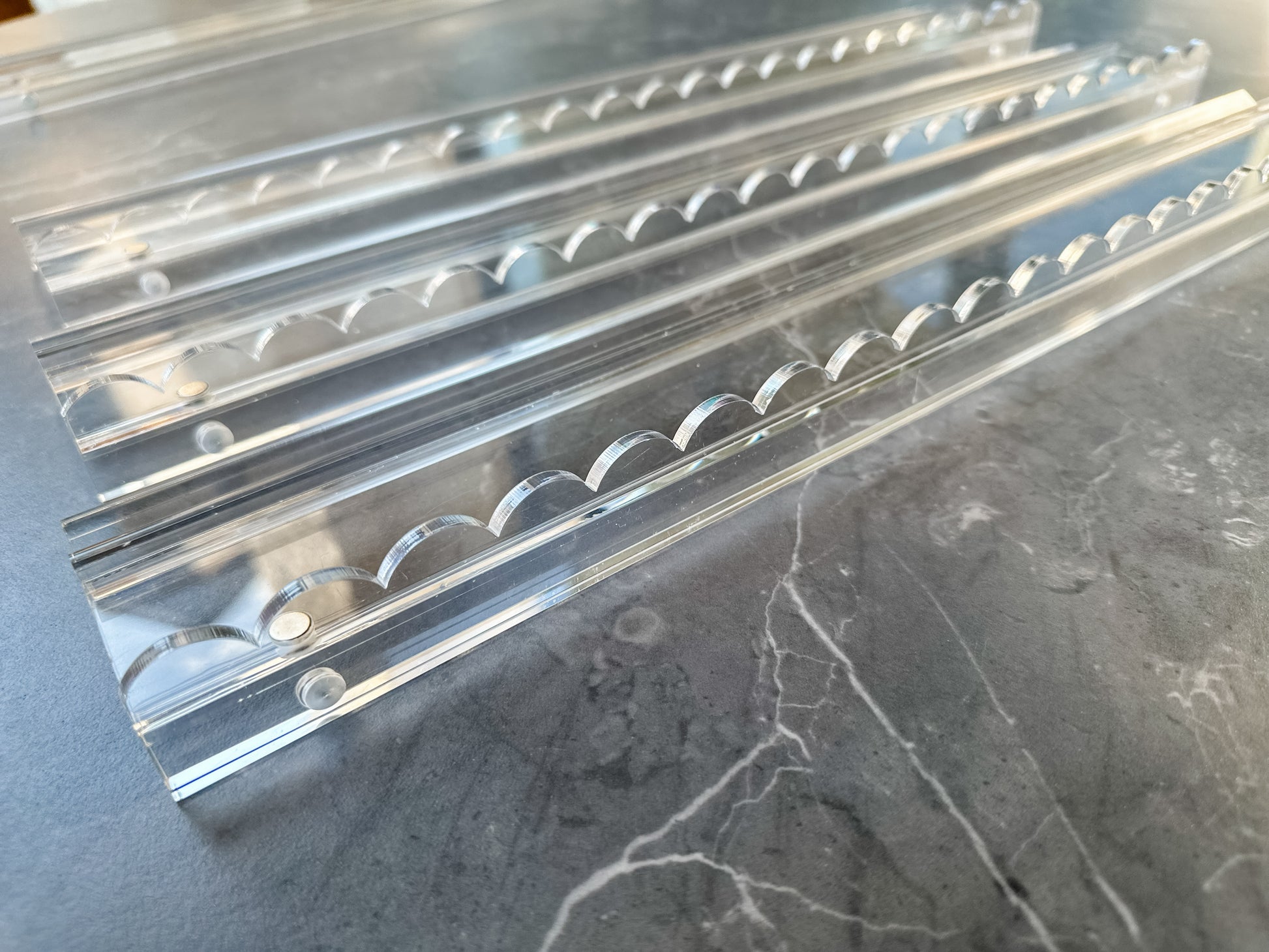 Close-up of Mahj Mood clear acrylic scalloped mahjong rack showing the scalloped pusher edge detail on a grey marble surface