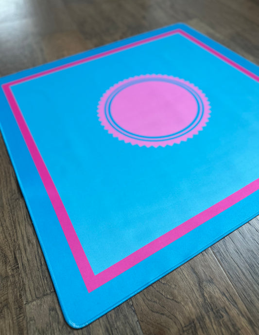Mahj Mood Pink Tide Glow Mat in electric blue with hot pink border and circular center design, laid flat on a wooden surface